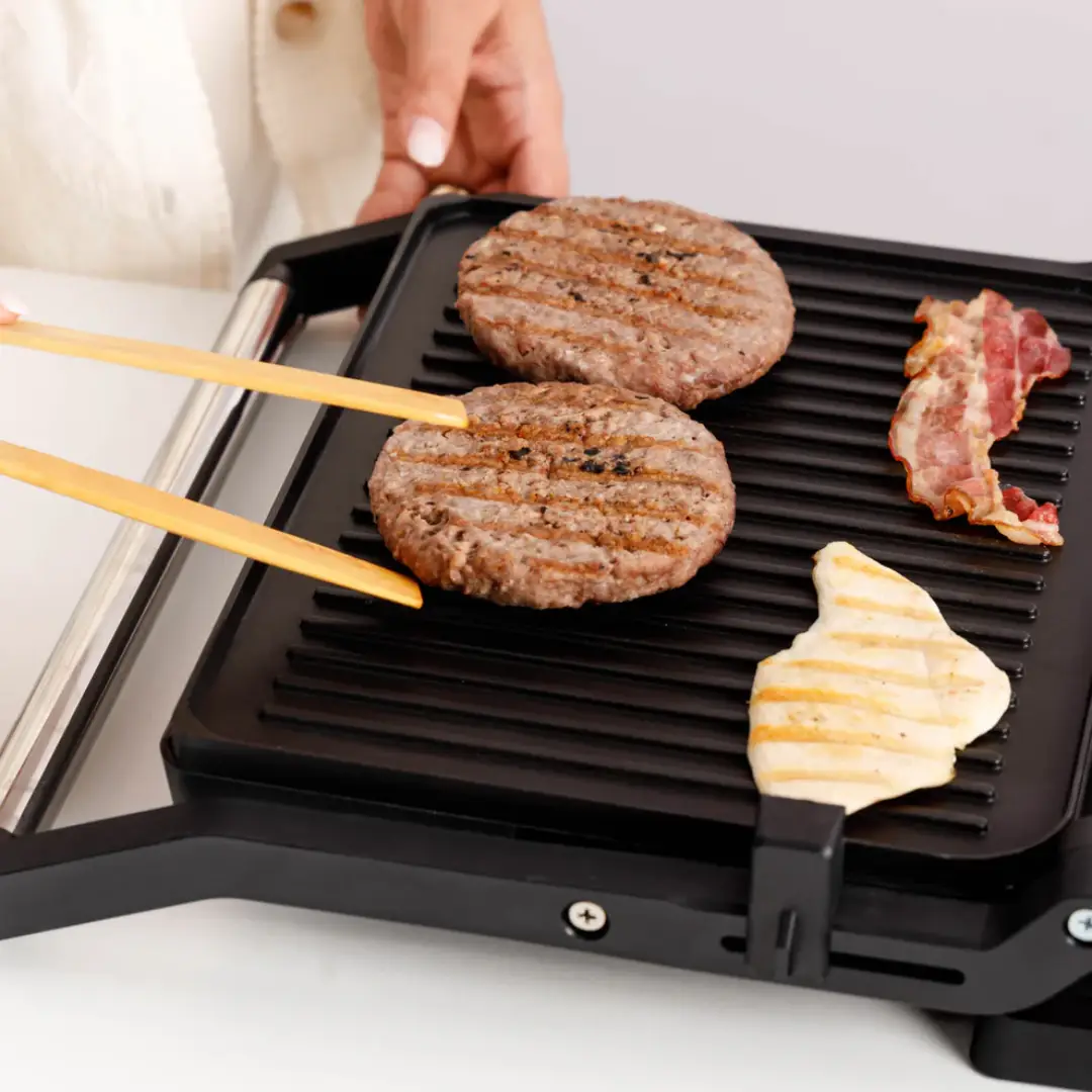 Imagen del grill Taurus Bistro Essential en funcionamiento, mostrando la cocción uniforme de los alimentos sobre sus placas antiadherentes con apertura 180º, disponible en Electrocash.